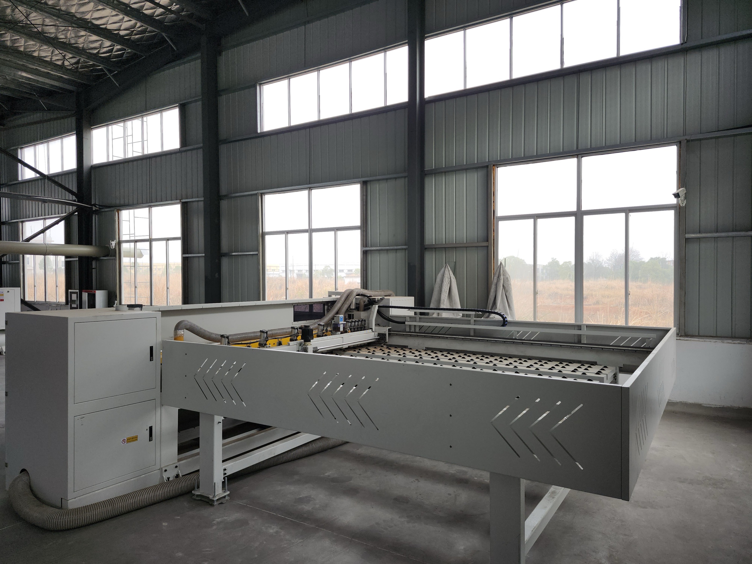 Long panel-processing machine positioned beside tall workshop windows