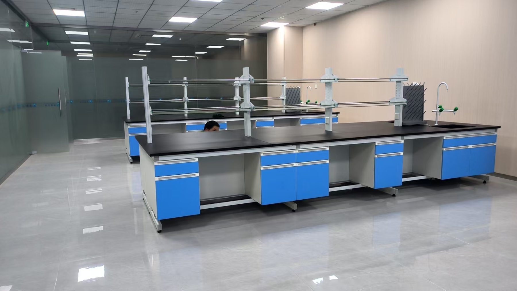 Double-sided laboratory island benches with sinks, service fixtures, drying racks, and overhead rails