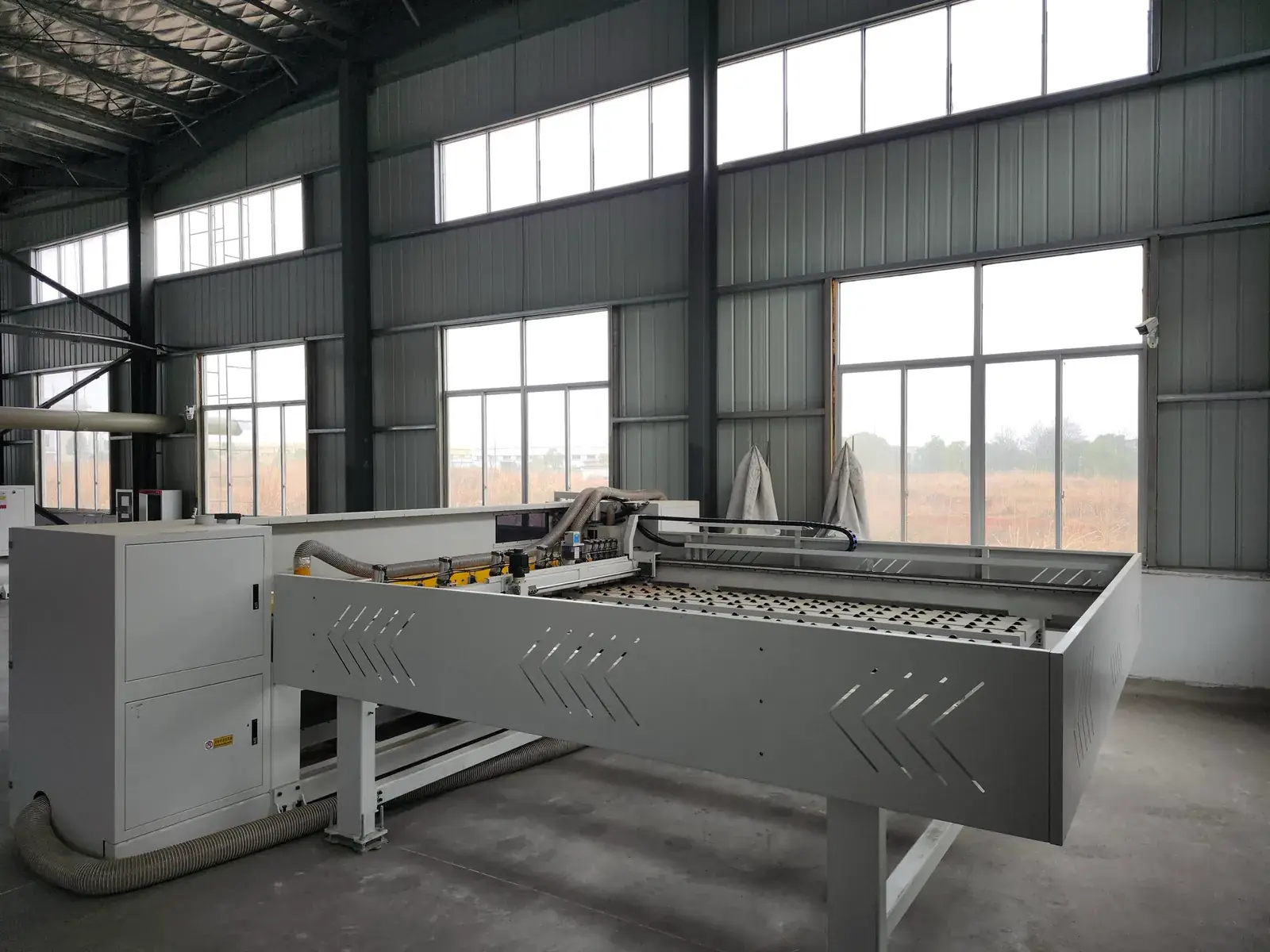 Long panel-processing machine positioned beside tall workshop windows